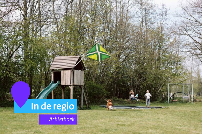 Een glijbaan en een trampoline op een grasveldje. Op de trampoline springen twee kinderen