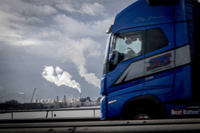 Een vrachtwagen passeert de stikstof uitstotende schoorstenen in de haven van Moerdijk.