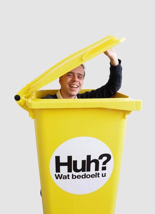 Bas Tebbe in een vuilnisbak met het logo van stichting ‘Huh? wat bedoelt u’